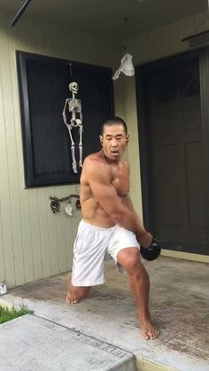 a shirtless man holding a kettle in front of a house