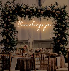 a table set up for a wedding with flowers and greenery on the wall behind it that says, there's always you