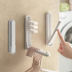 a person is pointing at the clothes hanger and toothbrush holder on the wall