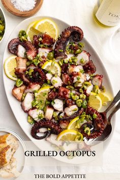 an octopus salad on a white plate with lemons and other food items around it