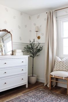 a white dresser sitting next to a window in a room with a rug on the floor