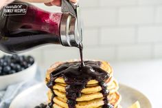 a stack of pancakes with blueberries and syrup being poured on top