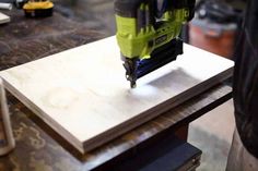 a power drill is being used on a piece of plywood that sits on a workbench