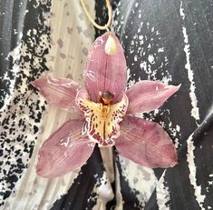 a pink flower is hanging on a black and white wallpapered background with an ornament attached to it