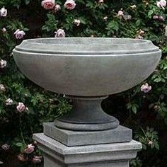 a large cement bowl sitting on top of a stone pedestal in front of some pink flowers