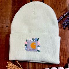 a white beanie hat with the letter c on it next to eggs and flowers