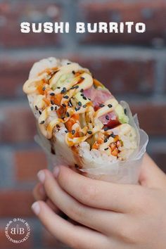 someone holding up a sushi burrito with toppings on it and the words sushi burrito written above it