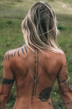 the back of a woman with tattoos on her upper body and lower back, standing in a grassy field