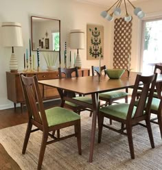 a dinning room table with green chairs in front of a large mirror and windows