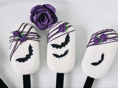 three halloween pops decorated with white chocolate and purple icing are sitting on a plate