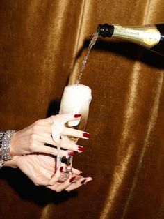 a woman's hand holding a wine glass and pouring it into a champagne bottle