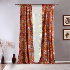 an orange floral curtain hangs in front of a window with white walls and flooring