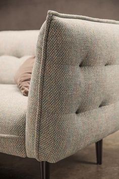 an upholstered chair with wooden legs and a cushion on the backrest, in front of a dark background