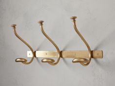 three brass - plated hooks hang on a gray wall