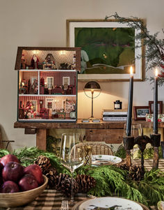 a christmas table setting with pine cones, apples and candles on the table in front of it