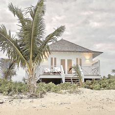 a small white house sitting on top of a sandy beach next to trees and bushes