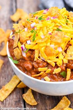 a white bowl filled with chili cheese and tortilla chips on top of a wooden table