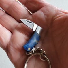 a hand holding a small blue and silver knife keychain in it's palm