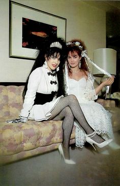 two women dressed in costumes sitting on a couch with one holding a lamp and the other wearing stockings