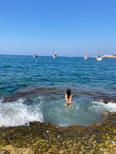 a woman wading in the ocean with sailboats in the background