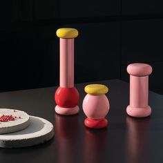 three pink and yellow vases sitting on top of a black table next to a cake