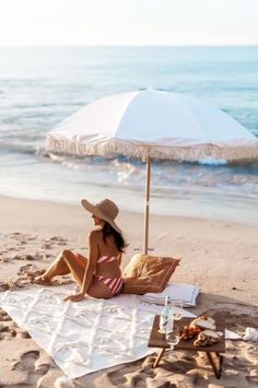 a woman laying on top of a towel under an umbrella at the beach next to the ocean