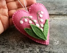 a hand holding a pink felt heart with green leaves and white flowers on the inside