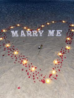 a heart made out of candles in the sand with words marry me written on it