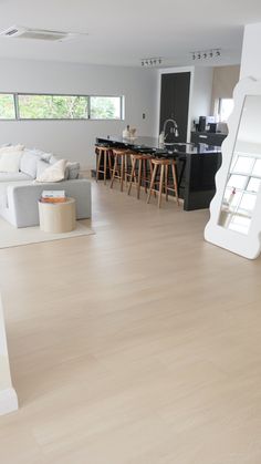 an open living room and kitchen area with hardwood flooring, white couches and bar stools