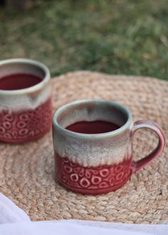 two coffee mugs sitting on top of a straw tablecloth next to each other