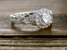 a white gold engagement ring with an oval center stone surrounded by small diamonds on a wooden surface