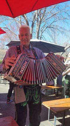 a man holding an accordion in front of his face and smiling at the camera while standing under red umbrellas