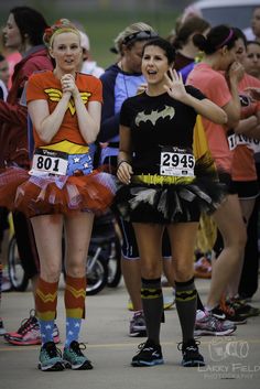 two women dressed up as batman and wondergirls at the start of a race