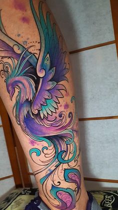 a colorful tattoo on the leg of a person with blue and purple feathers flying over them