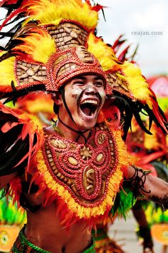 a man in a colorful costume with feathers on his head and chest, smiling at the camera