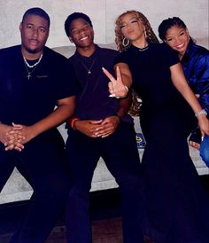 four people posing for a photo in front of a white wall with one person making the peace sign