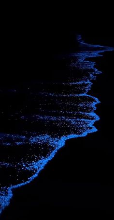 the ocean is dark and blue with waves coming in from the shore at night time