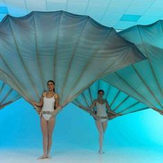 three women in white leotards are standing under large blue paraphernalia