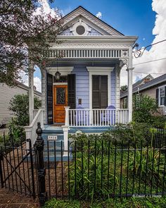 a small blue house with white trim and black iron fence around it's front door