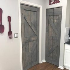 two wooden doors in a kitchen with utensils hanging on the wall next to them