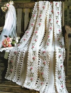 a white crocheted blanket sitting on top of a wooden bench next to flowers