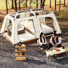 two people sitting in chairs near a tent with a bed and table on the ground