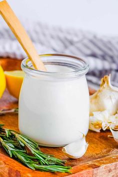 a jar of yogurt sitting on top of a wooden cutting board next to lemons and garlic