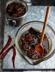 a glass bowl filled with food next to a jar of chili sauce and a wooden spoon