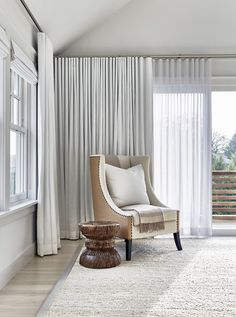 a living room with white curtains and a chair