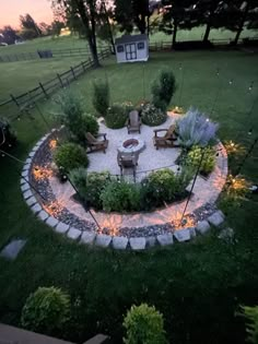 an outdoor fire pit surrounded by grass and rocks in the middle of a yard at dusk