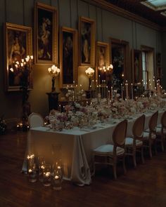 a long table with candles and flowers on it in a room filled with pictures, paintings and chandeliers