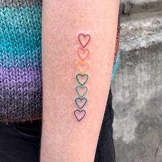 a person with a tattoo on their arm that has hearts painted on it and the word love written in rainbow colors