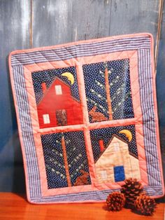 a quilted wall hanging on the side of a wooden table next to a pine cone