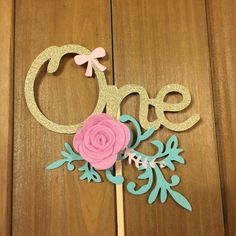 a cake topper with the word one on it and a pink flower in the middle